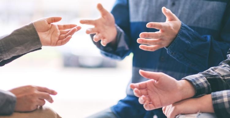 Close-up of several people’s hands gesturing toward each other during a conversation, suggesting discussion or collaboration.
