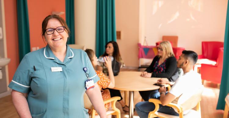 Hospital worker in a room full of patients and family members smiling at the camera