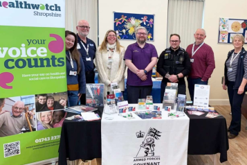 a group of adults gathered around a table displaying leaflets and banners from the Armed Forces Covenant and Healthwatch Shropshire