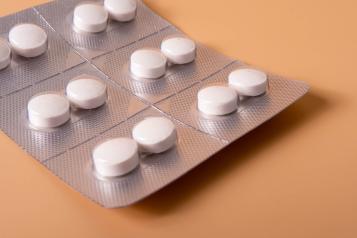 Blister pack of white round tablets arranged in a grid on a silver foil strip against a warm orange background.