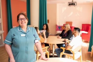 Hospital worker in a room full of patients and family members smiling at the camera