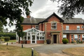 A large brick building with windows and conservatory set in gardens