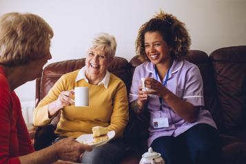 two old women in a care home laughing with their nurse