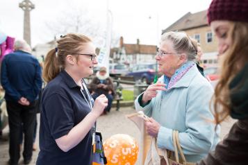 A female volunteer talking to an elderly lady at a community event.