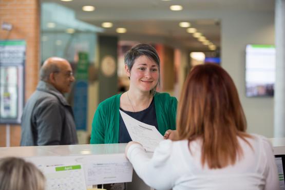 Woman speaking to a receptionist in a health centre Woman speaking to a receptionist in a health centre