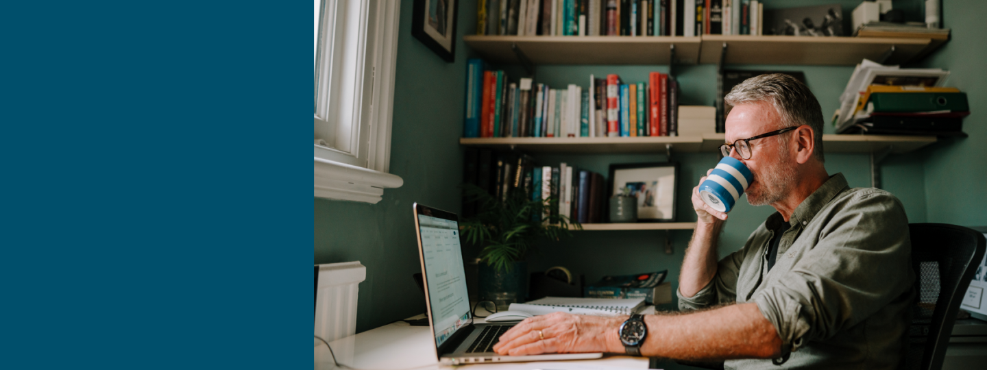man in his home office completing a survey on his laptop while drinking a cup of tea or coffee