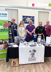 a group of adults gathered around a table displaying leaflets and banners from the Armed Forces Covenant and Healthwatch Shropshire