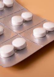Blister pack of white round tablets arranged in a grid on a silver foil strip against a warm orange background.