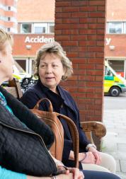 Two older women sat on a  bench talking outside a hospital