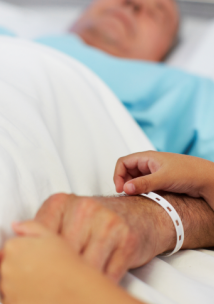 man lying down in a hospital bed with a child holding his hand
